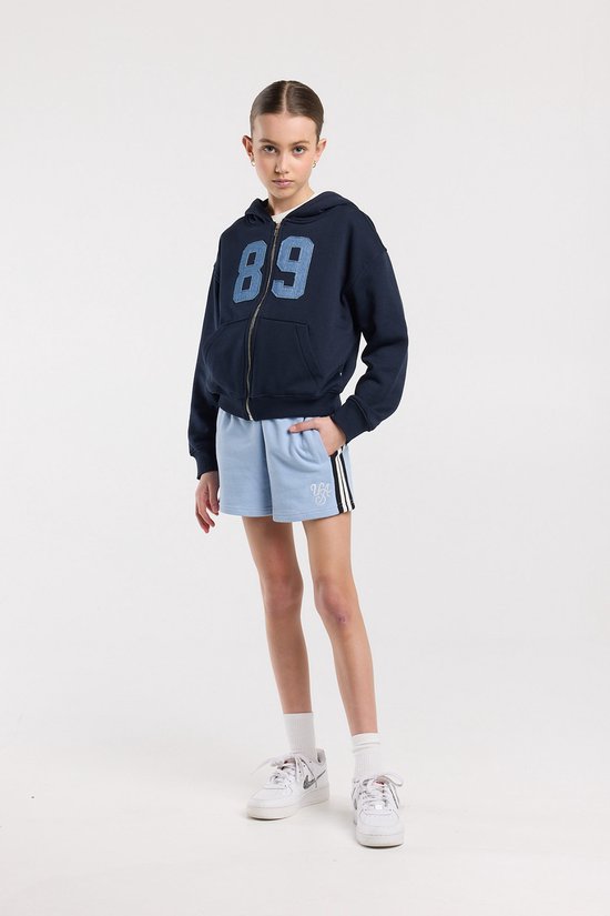 Mannequin portant un short bleu clair avec rayures latérales, un imprimé monogramme blanc, des chaussettes blanches et des baskets blanches.