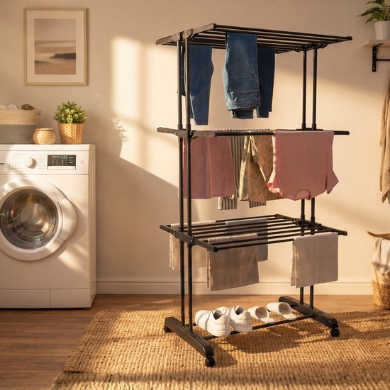 Zwart, drielaags droogrek met jeans, shirts en handdoeken. Een wasmachine staat links. Een jute vloerkleed ligt onder het rek.