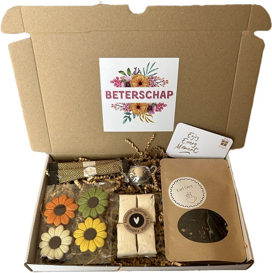 Een open geschenkdoos met 'Beterschap' erop, bevat bloemvormige chocolades, thee, nougat, honing en een kaartje.