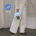 Een persoon in witte broek en gestreepte blouse houdt een lichtgewicht, wit en grijs airco-apparaatje vast met een blauwe gloed.