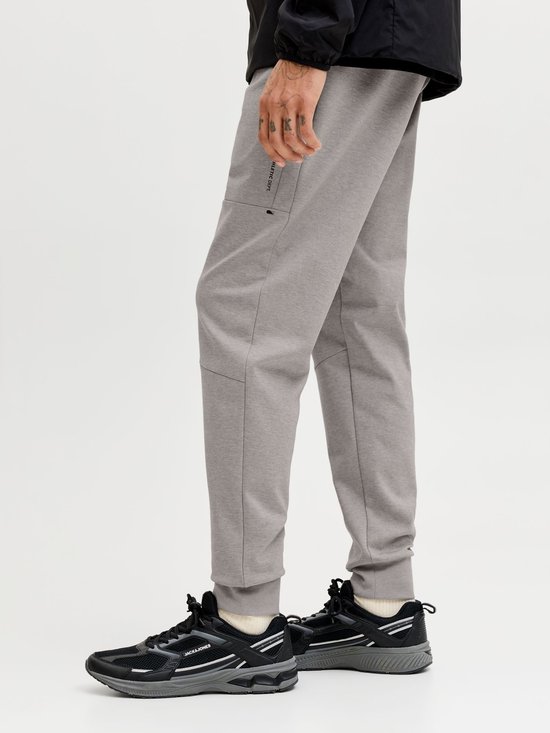 Grijze joggingbroek met ritsvak en 'JJ Athletic Dept.' opdruk, gedragen met zwarte sneakers.