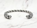 Zilverkleurige, gedraaide armband met drakenkopuiteinden op een marmeren achtergrond.