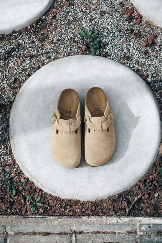Een paar beige suède Birkenstock Boston klompen op een ronde betonnen ondergrond.