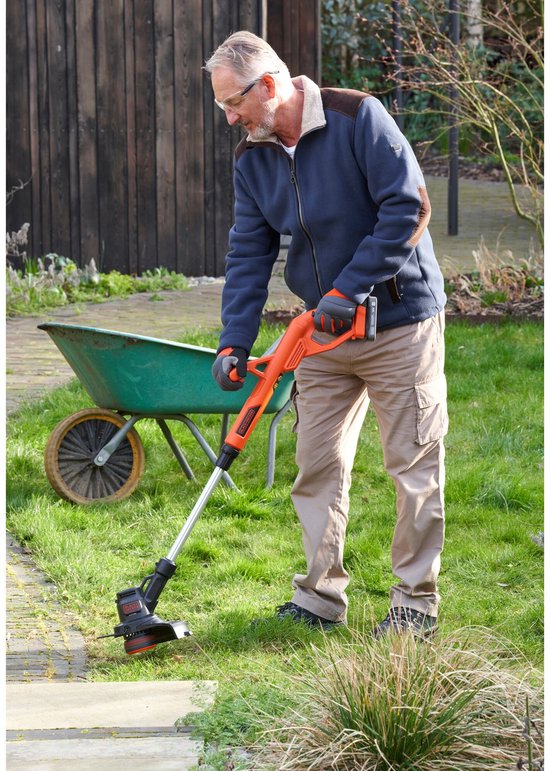 Een oudere man met veiligheidsbril trimt gras met een oranje grastrimmer.