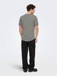 Man met grijze T-shirt en zwarte jeans, achterkant. Grijze T-shirt met ronde hals. Zwarte jeans met wijde pijpen.