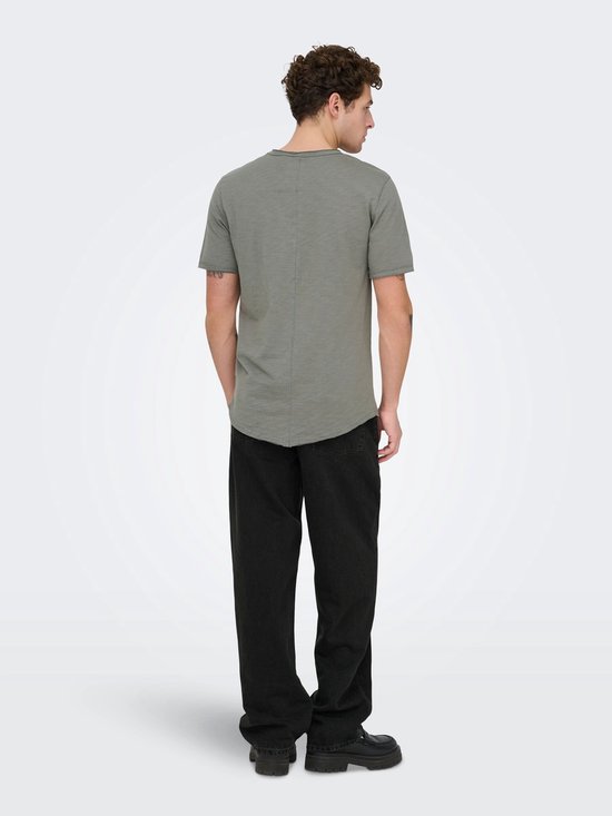 Man met grijze T-shirt en zwarte jeans, achterkant. Grijze T-shirt met ronde hals. Zwarte jeans met wijde pijpen.