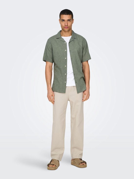 Model draagt groen, kortemouwige hemd met linnen textuur en beige broek.