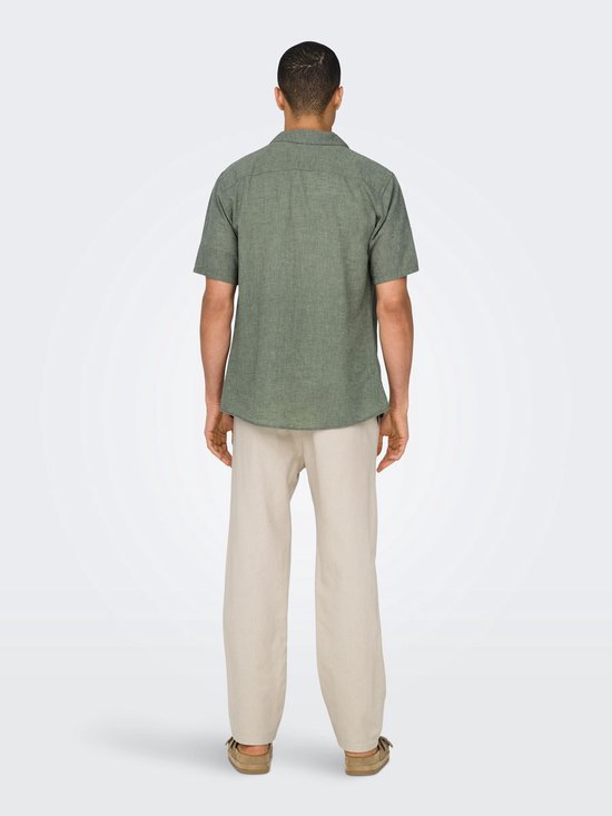 Man draagt groen, kortemouwige hemd met linnen textuur en beige broek.