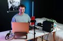 Man met laptop en DJ-controller in een kamer met neonverlichting en posters.