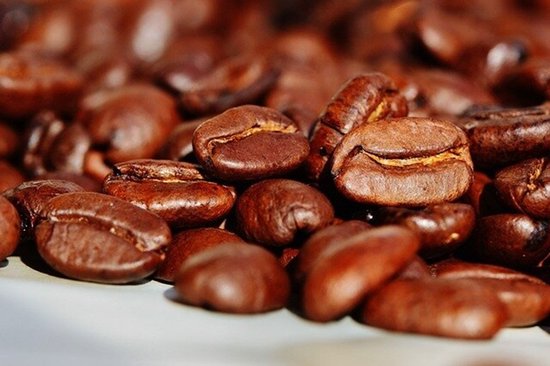 Gedetailleerde macro-opname van geroosterde koffiebonen met een bruine, glanzende textuur.