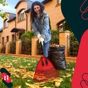 Vrouw met spijkerjas en witte handschoenen gebruikt rode bladhark bij een vuilniszak.
