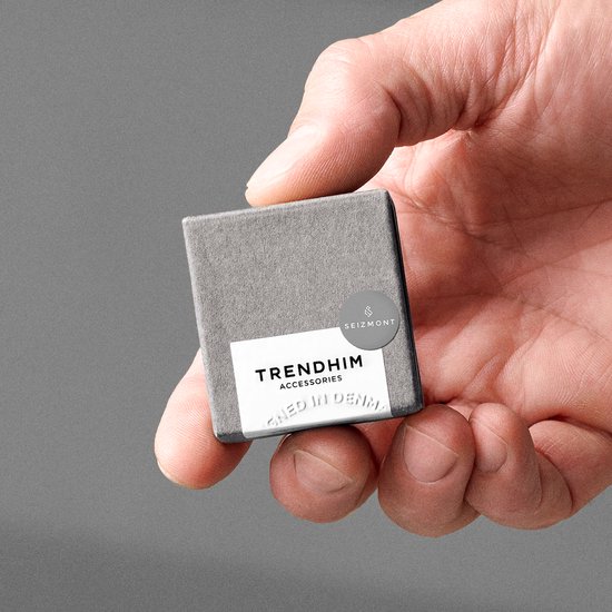 Hand die een kleine grijze doos met 'TRENDHIM ACCESSORIES' label vasthoudt.