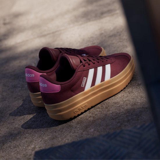 Bordeauxrode Adidas sneakers met witte strepen, bruine zool en roze accenten.