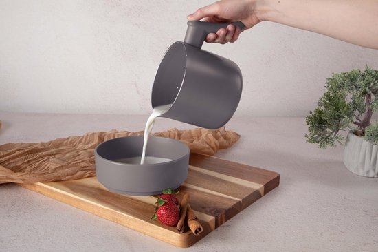 Hand die grijze melk uit een grijze melkpan in een grijze kom schenkt.