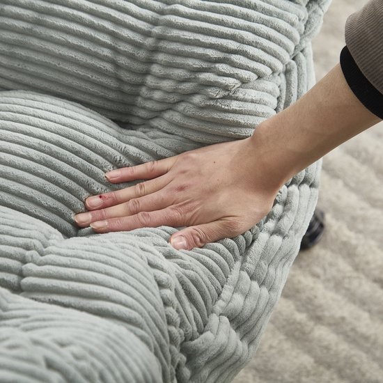 Hand rust op de zachte, lichtgroene corduroy stof van een loungestoel.