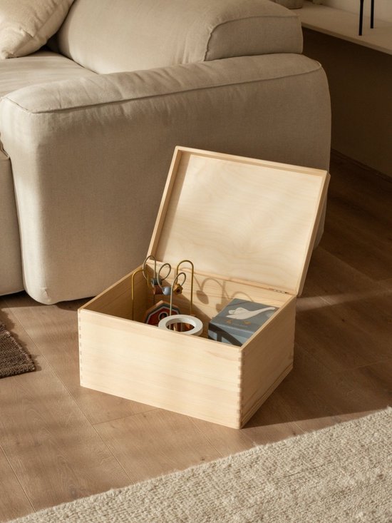Een open houten kist, gevuld met kinderspeelgoed, naast een bank.