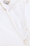 Detail van de tailleband van een crèmekleurige jeans met een knoop en beige stiksels.