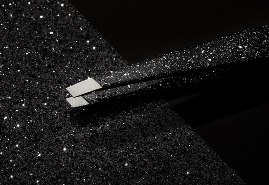 Schuine punten van een zwarte glitter pincet op een glinsterende zwarte ondergrond.