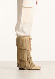 Model draagt een beige suède laars met franjes.
