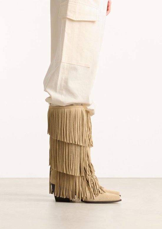 Model draagt een beige suède laars met franjes.