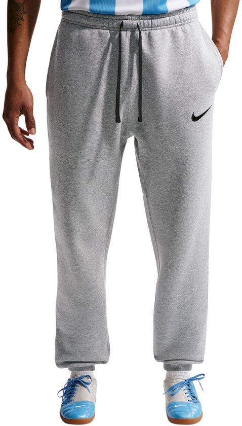 Grijze joggingbroek met zwarte Nike Swoosh, gedragen door een model met een gestreepte top en voetbalschoenen.