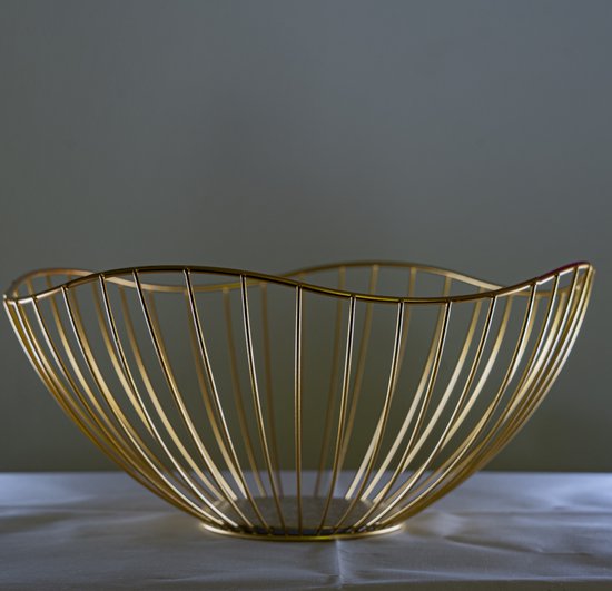 Gouden fruitschaal met verticale spijlen en een golvende rand, op een witte doek.