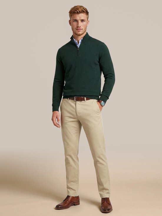 Homme portant un pull en laine mérinos vert foncé avec fermeture éclair à la gorge, associé à un chino beige et des chaussures marron.