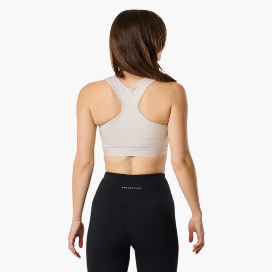 Model van achteren gezien, draagt een lichte sportbeha met racerback en zwart met logo-band en een zwarte legging met logo.