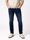 Model in een donkerblauwe jeans met vijf zakken en lichte wassing. De broek heeft een regular fit. Grijze sneakers.