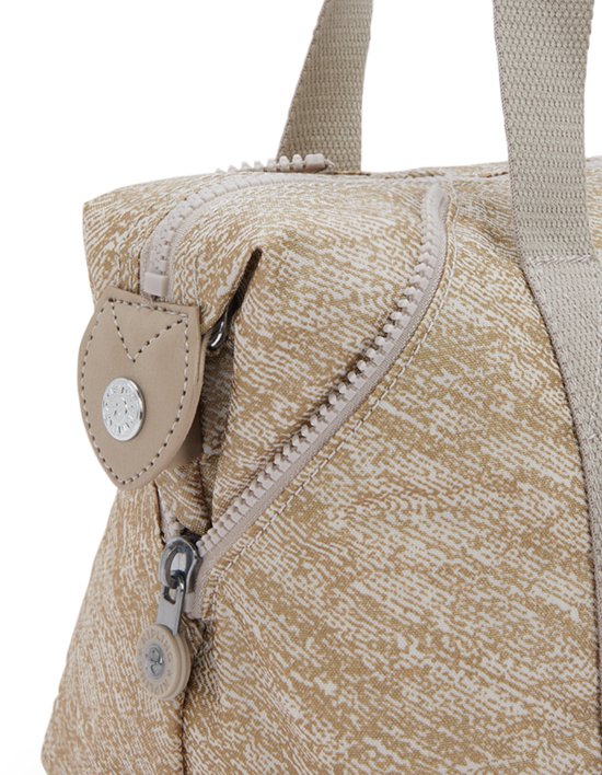 Close-up van een beige tas met goudkleurige spikkelprint en beige stoffen handvatten en ritsen.