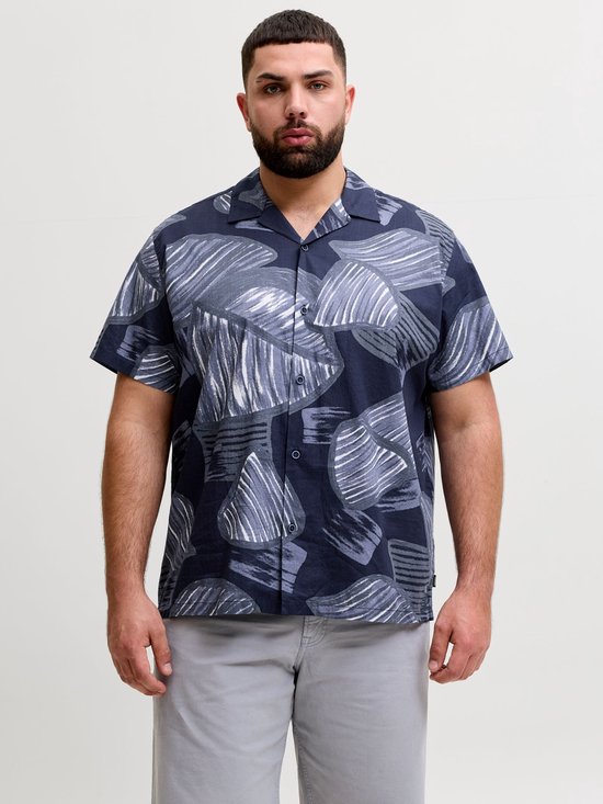 Model in een blauw overhemd met abstracte bladprint, gedragen met een grijze korte broek.