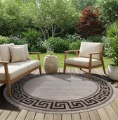 Rond grijsbeige vloerkleed met zwart zigzagpatroon, geplaatst op een houten terras met tuinmeubilair.