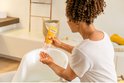 Vrouw met krullend haar die Weleda baby calendula shampoo & douchecrème in een babybadje doet.