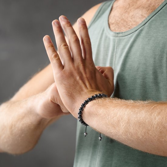 Een man met een groene tanktop, close-up van zijn pols met een donkergrijze, glanzende hematiet kralen armband.