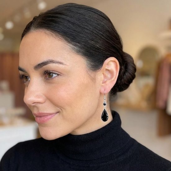Vrouw met opgestoken haar en zwarte coltrui draagt zilverkleurige oorbel met zwarte druppelvormige hanger.