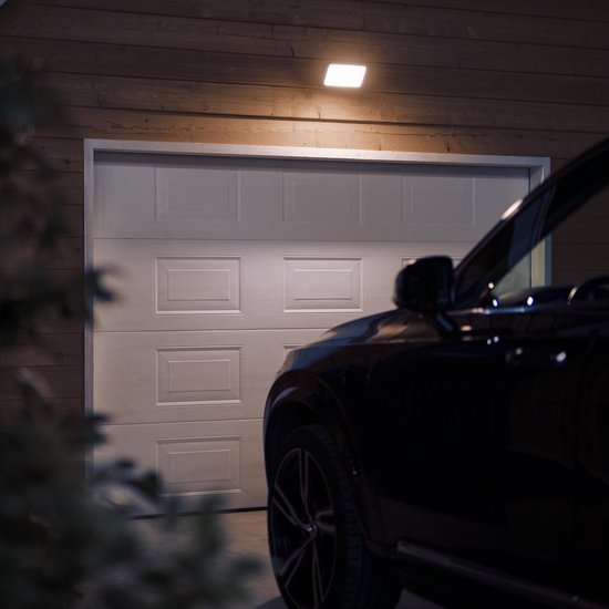 Zwarte auto voor een witte garagedeur, verlicht door een Philips Hue buitenlamp.