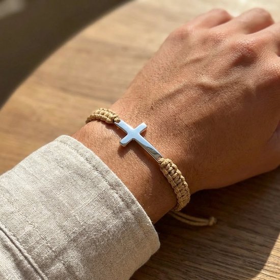 Beige gevlochten armband met zilverkleurig kruis om een mannenpols.