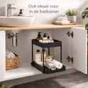 Zwarte, uitschuifbare organizer met twee niveaus, gevuld met badkamerproducten zoals zeep, lotions en handdoeken.