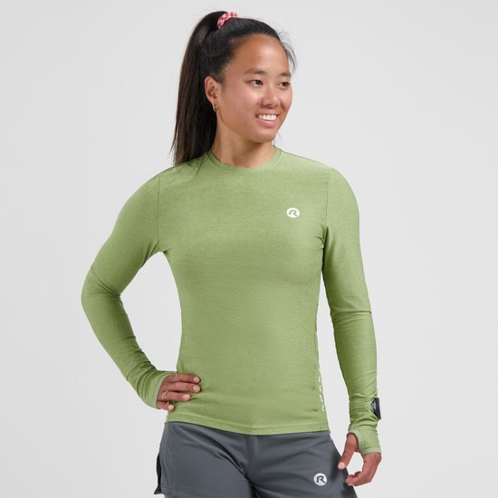 Model in een groen, langemouwen sportshirt met duimgaten, witte logo op de borst.