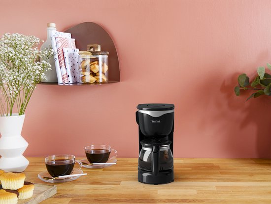 Cafetière Tefal noire sur un plan de travail en bois, avec deux tasses de café à côté.
