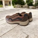 Bruine leren Rieker sneakers met ritssluiting aan de zijkant, zittend op een stenen ondergrond.