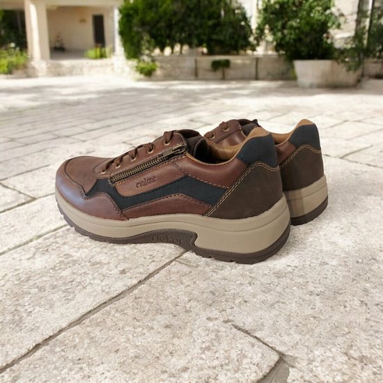 Bruine leren Rieker sneakers met ritssluiting aan de zijkant, zittend op een stenen ondergrond.