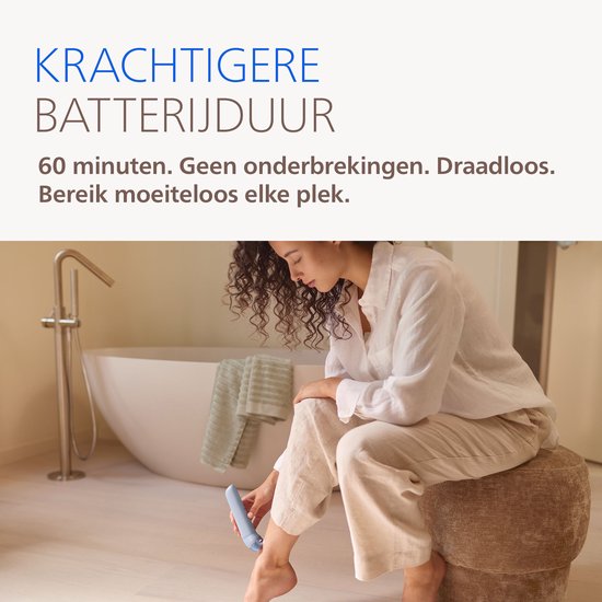 Vrouw in badkamer zit op poef en epileert haar been met lichtblauwe Philips epilator
