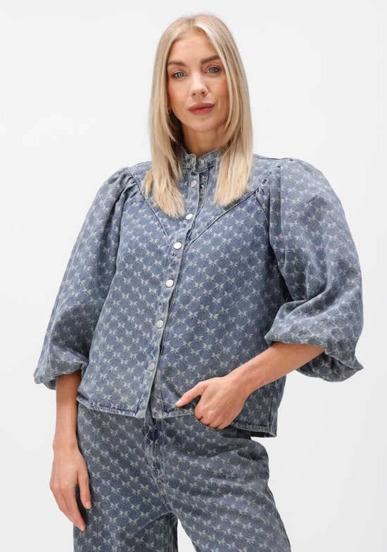 Model in een lichtblauwe denim blouse met pofmouwen, een opstaande kraag en een subtiel sterpatroon.