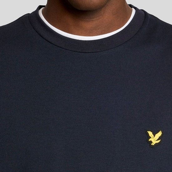Detail van de donkerblauwe trui met ronde hals en geel Lyle & Scott logo op de borst.