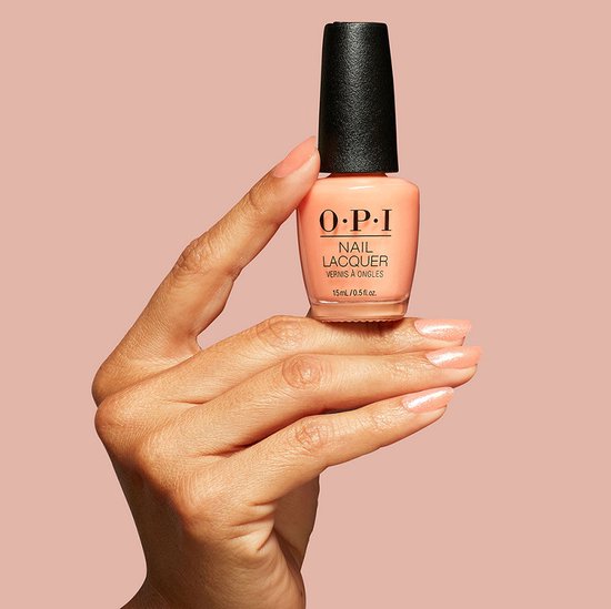 Hand met een zachte perzikkleurige nagellak, die een flesje OPI nagellak vasthoudt.