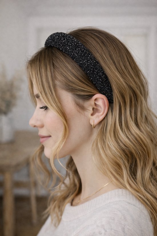 Model met blonde haren draagt een zwarte glitter haarband.