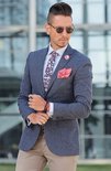 Man met blauw jasje, bloemen das, rode pochet en een leren armband met zwarte en rode strengen.