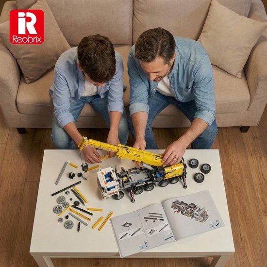Een vader en zoon bouwen samen aan een gedetailleerde, gele en witte mobiele kraan op een tafel, met instructieboekjes.