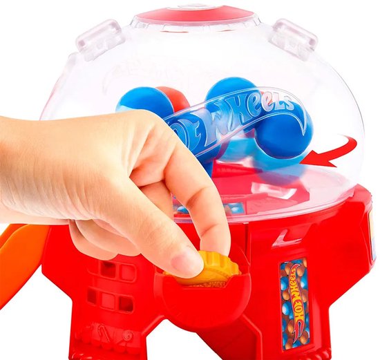 Hand plaatst muntje in rode snoepautomaat met blauwe Hot Wheels ballen